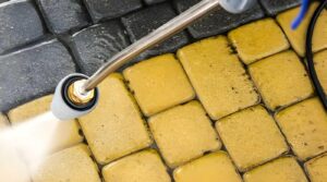 High-pressure water cleaning sandstone pavers, removing dirt and grime to restore the natural stone color.