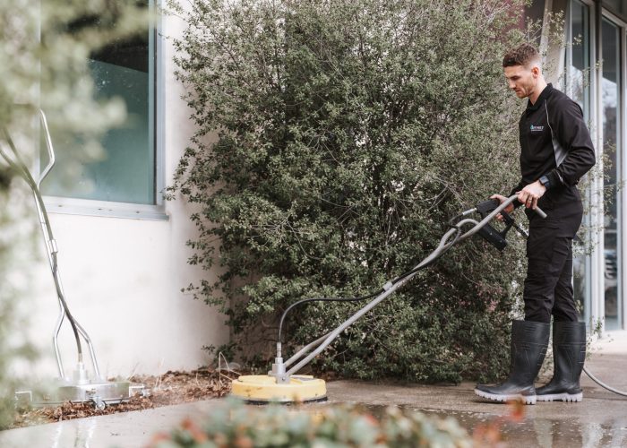 A professional pressure washing technician cleaning a driveway with high-pressure water jetting equipment